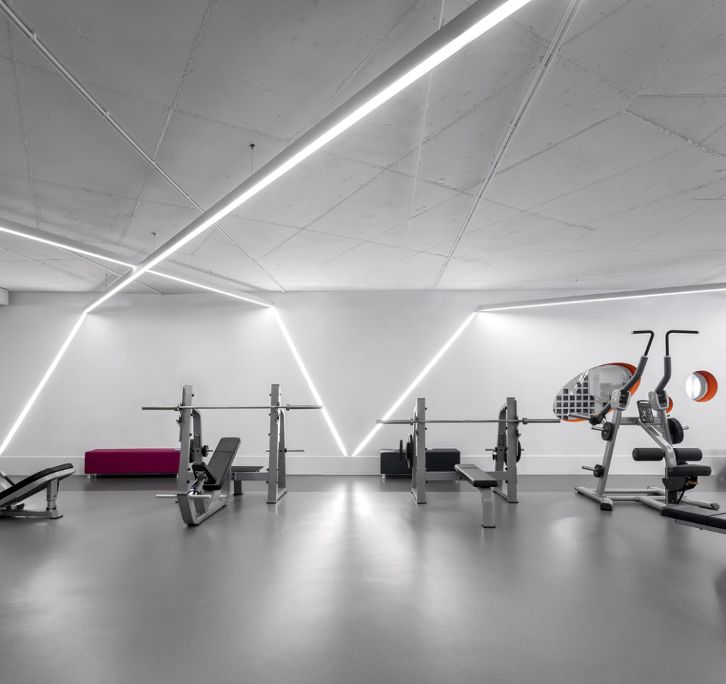 A combination of recessed linear wall lighting and linear suspension ceiling lights creates a dynamic, organic design in a gym.