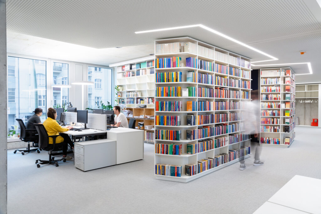 Linear recessed lighting follows the perimeter of a winding set of bookcases in a library