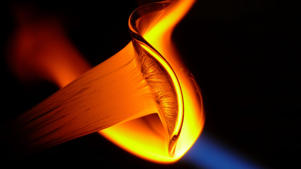Glass being heated under a blue flame, turning from red to yellow