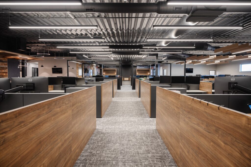 Linear LED pendant lights illuminate rows of cubicles in a modern office.
