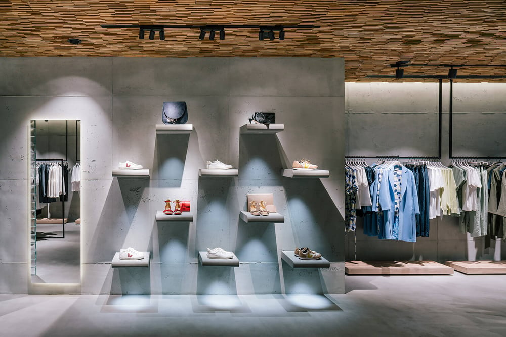 A black three-light track lighting system directs light at a wall displaying shoes and accessories in a retail clothing store.