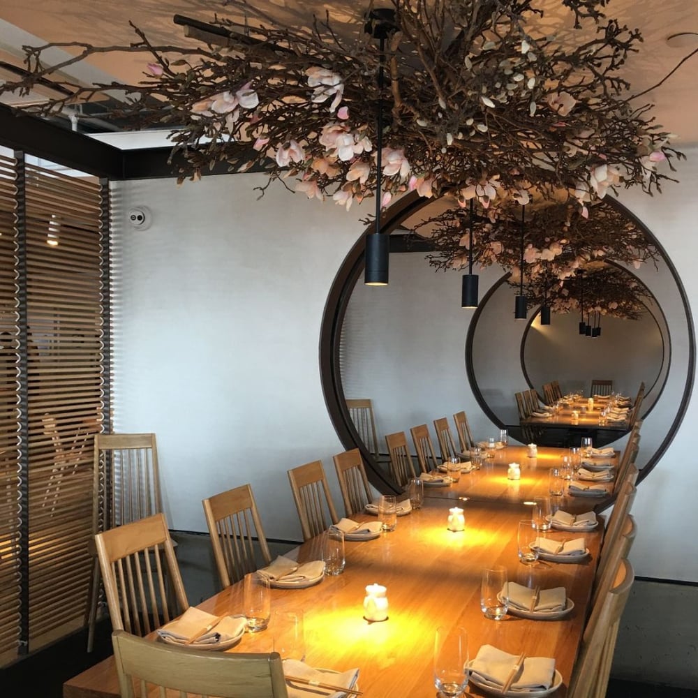 Black ceramic pendant lights adorn a restaurant table from a suspended cherry blossom floral arrangement.