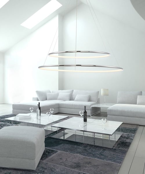 A two-tier round chandelier with a silver finish suspended from a sloped ceiling over a coffee table in a modern living room.