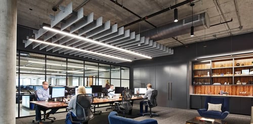 Acoustic linear pendant lighting suspended over an office conference room workspace with cylinder downlights over a common area