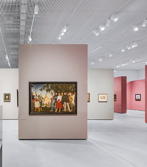 Recessed track light channels fitted with monopoint spotlights and linear surface-mount lights showcase paintings in an art gallery.