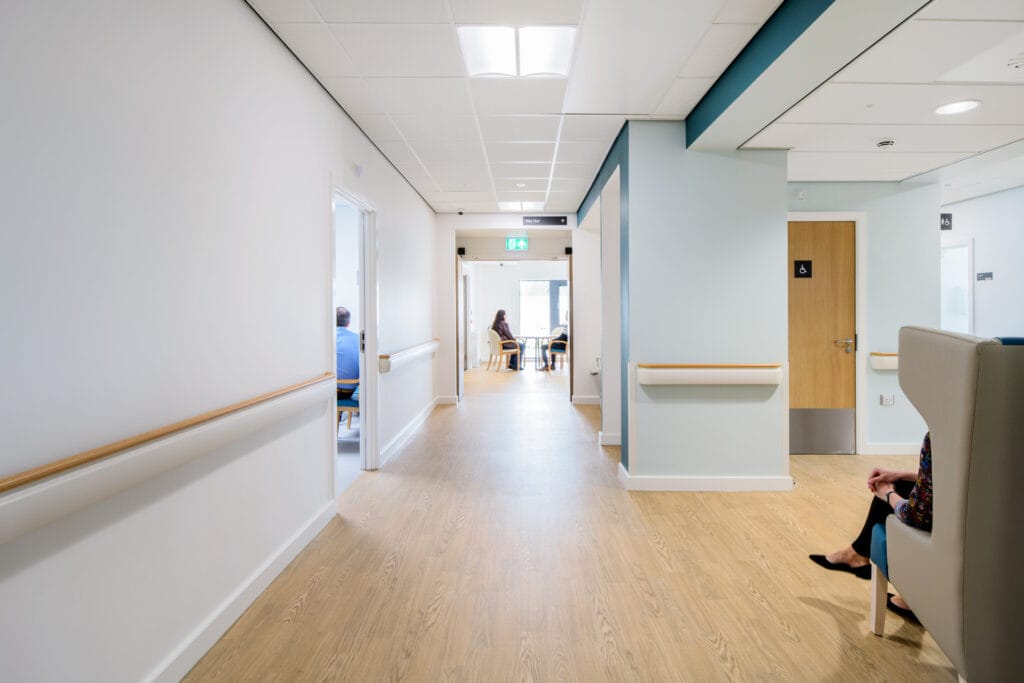 A hospital hallway lit with troffer lights that feature a vertical reflector to provide indirect downlight that reduces harsh glare.
