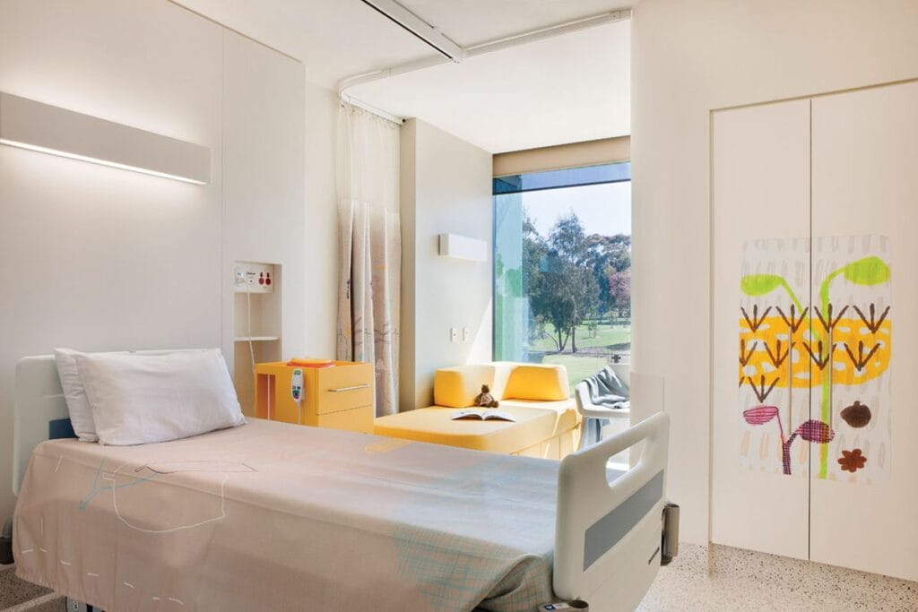 A child's hospital room features linear wall lights that provide direct and indirect light to reduce glare and balance with natural light coming through a window