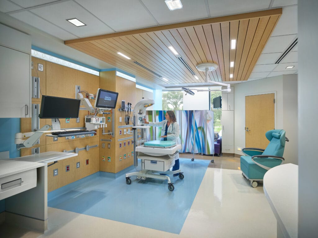 A healthcare professional works in a daylight-filled treatment room with recessed ambient lighting and adjustable examination lights.
