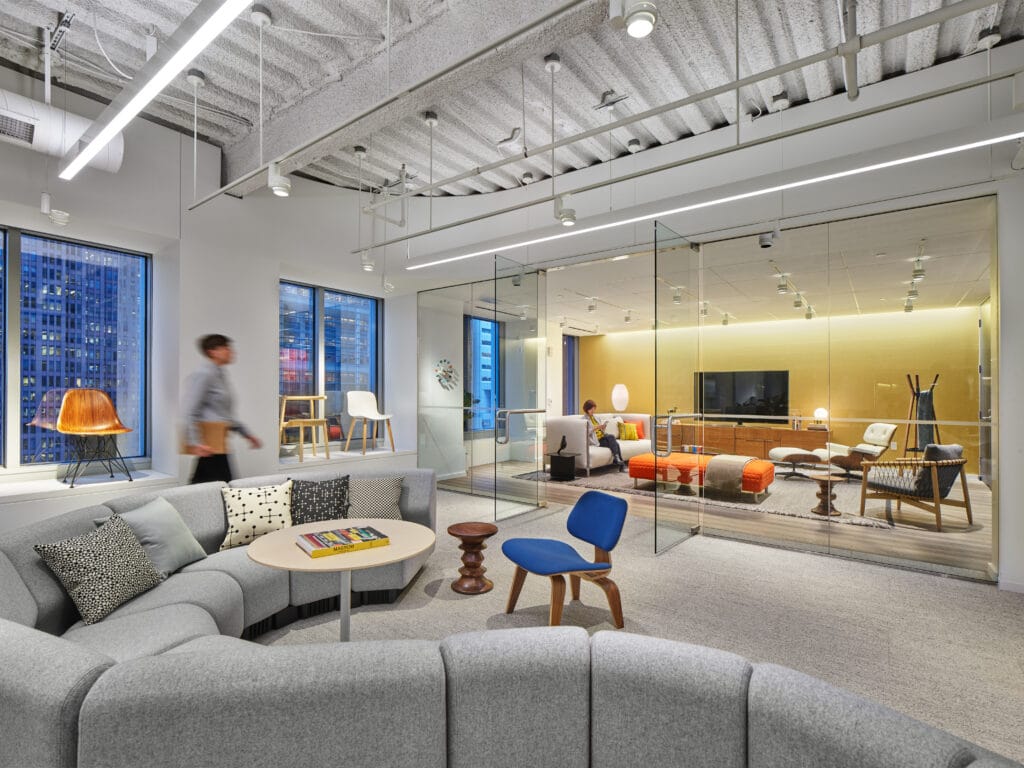 Suspended linear pendants, track lights and cove lighting illuminate an open office with daylight from floor-to-ceiling windows.