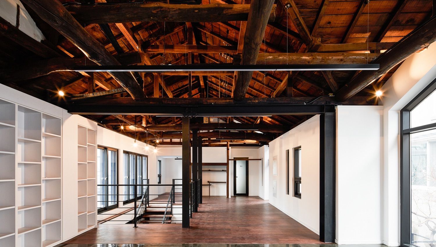 Linear pendant lights run the width of a corridor, providing uplighting to highlight the beams of peaked wood ceiling.