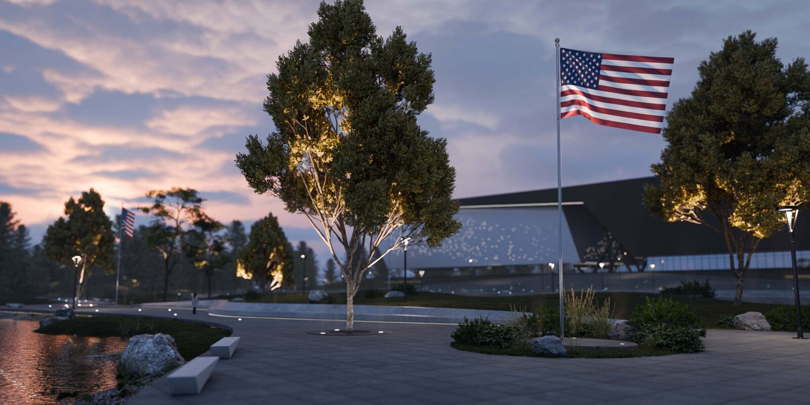Alcon 9094 LED in-ground uplights illuminating an American flag on a flagpole in a landscaped plaza setting at dusk.