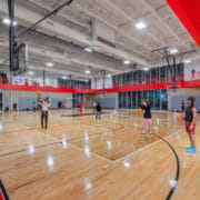 Suspended linear LED lights illuminate a large indoor gymnasium at Texas A&M University.