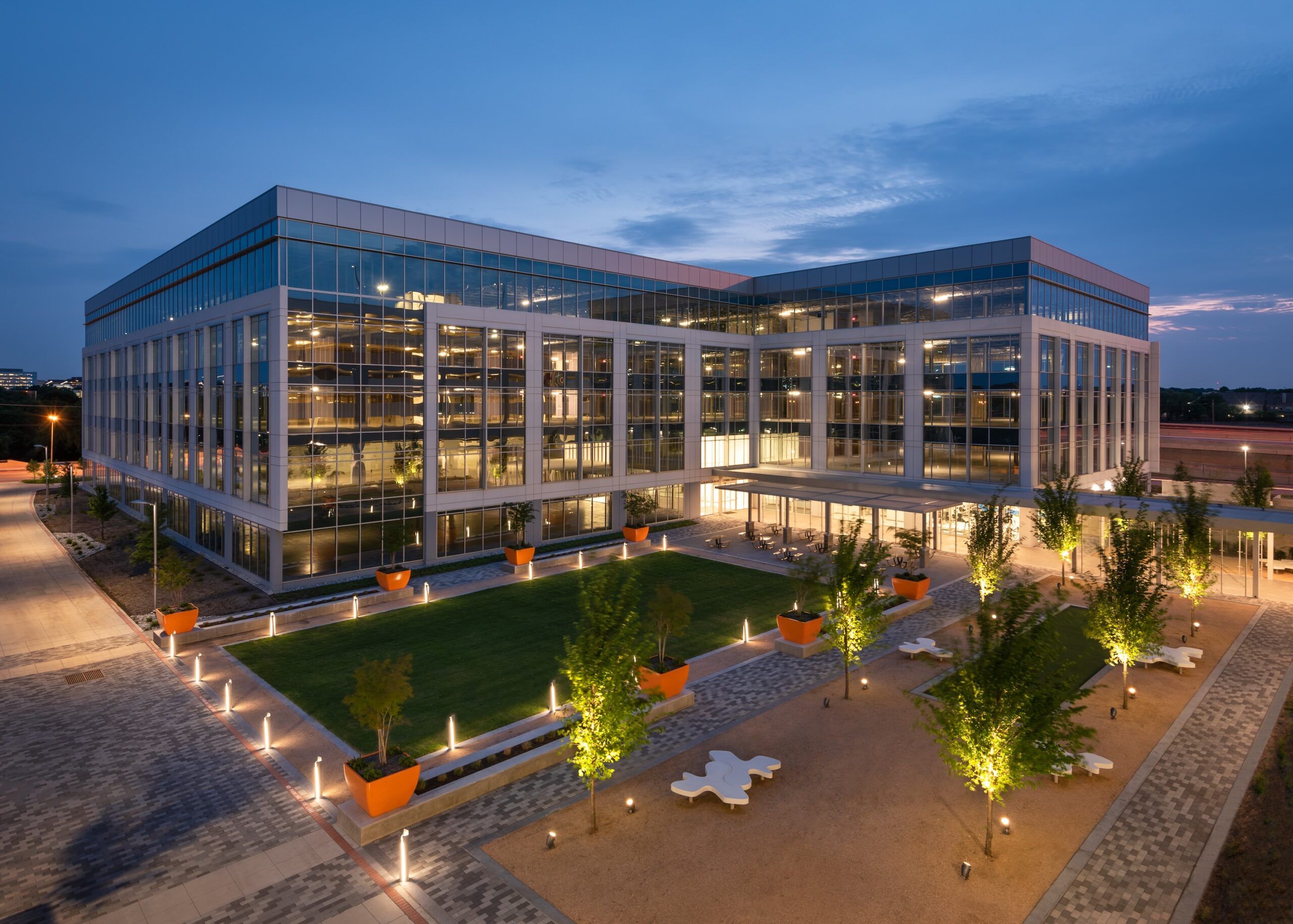 Bollard lights illuminate pathways while directional uplights light trees at a corporate office plaza.