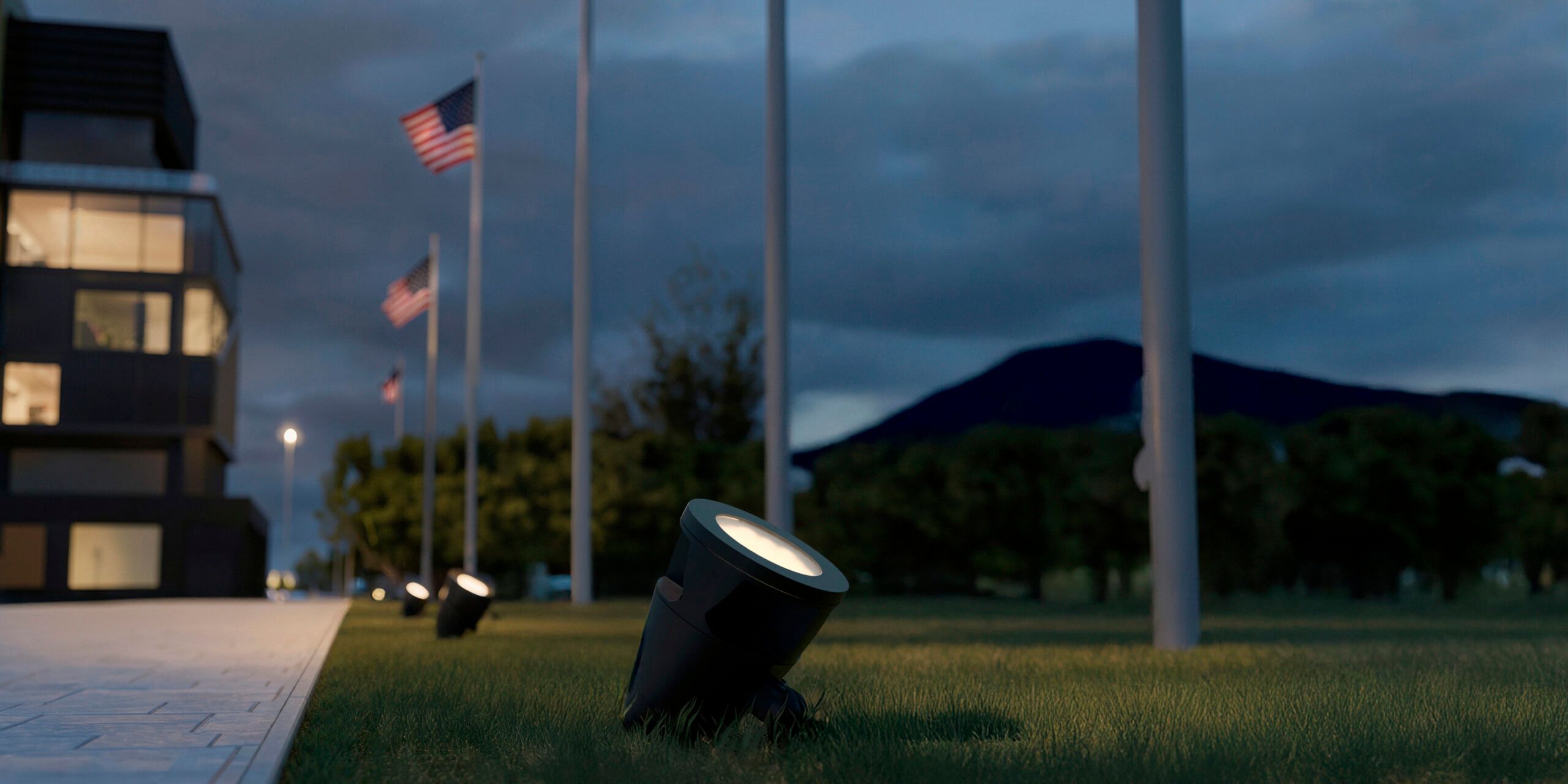 Alcon 9171 LED landscape spotlights installed in the grass and aimed upward to illuminate American flags on flagpoles at night.