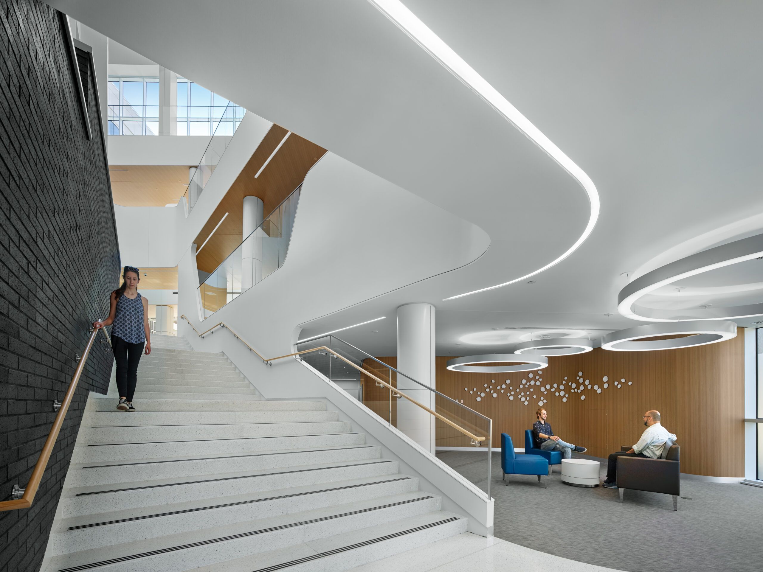 Kennedy Health lobby with curved linear lighting, ring pendants, a stairway and illuminated seating areas.