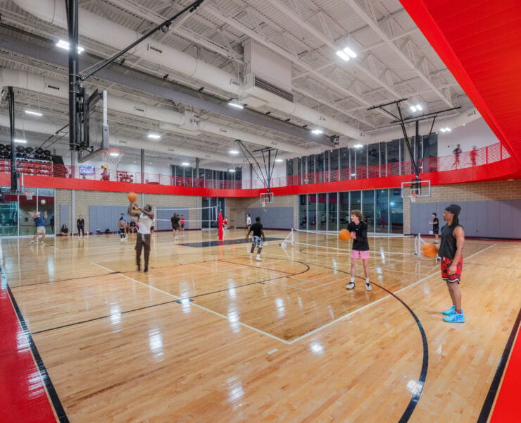 Suspended linear LED lights illuminate a large indoor gymnasium at Texas A&M University.