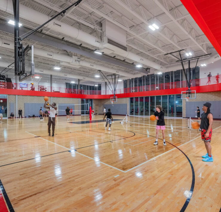 Suspended linear LED lights illuminate a large indoor gymnasium at Texas A&M University.