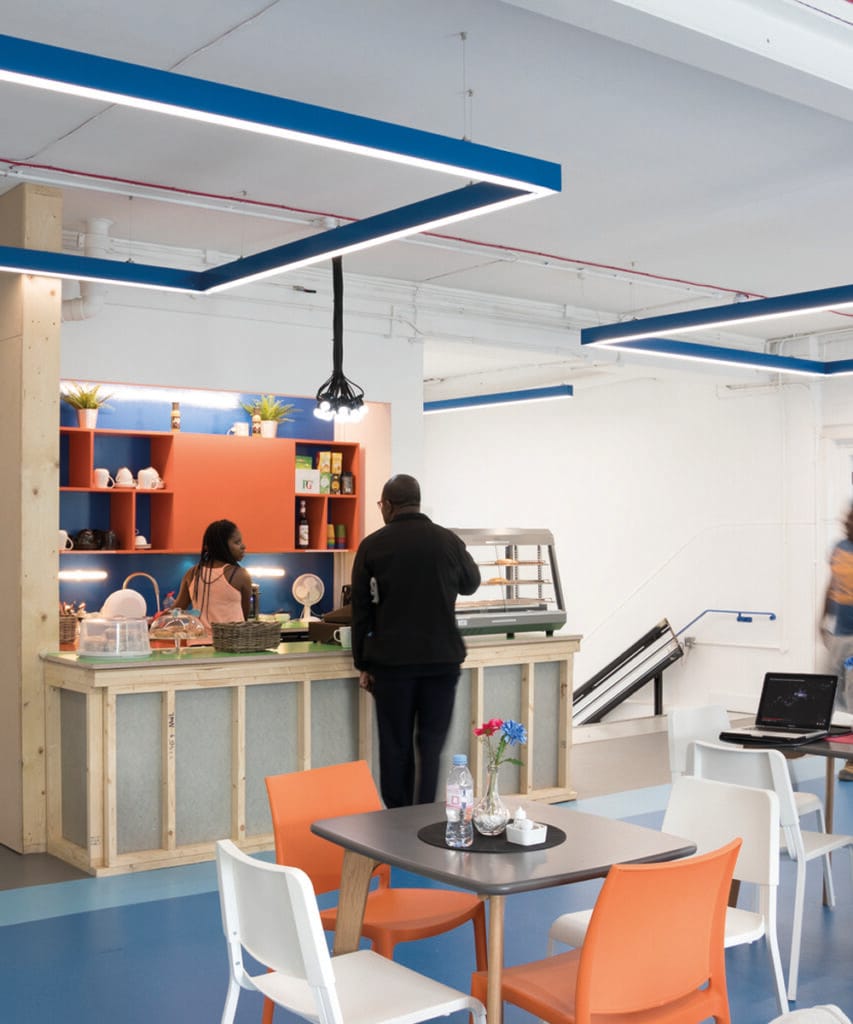 A retail cafe in an office building has blue rectangular pendant lights to match the accent wall and floor color used in the space 