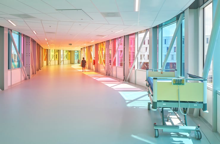 Recessed lighting with color tuning down this hospital hallway creates a color spectrum effect as people walk down the hall