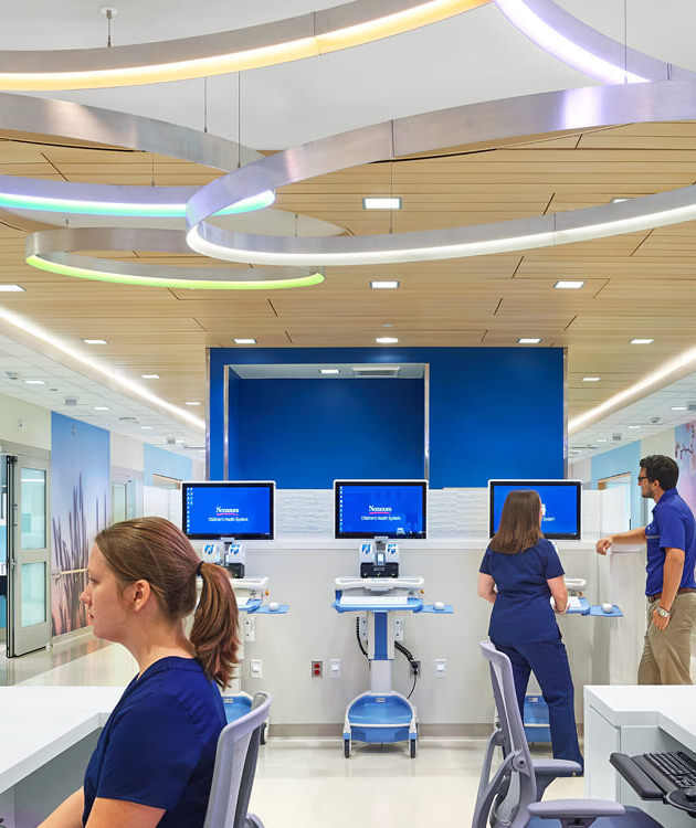 Modern ring pendant lights suspended at angles with soft pastel RGBW illumination above a hospital nurses’ station.