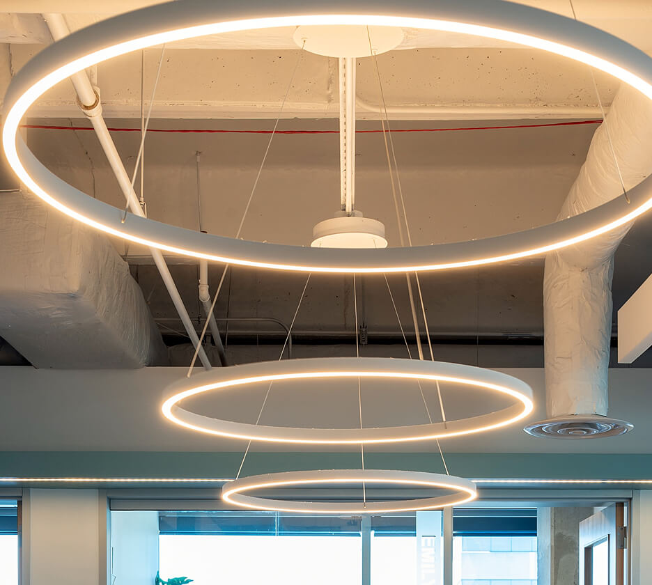 Three slim ring pendant LED lights reduce glare over office workstations with soft direct and indirect lighting.