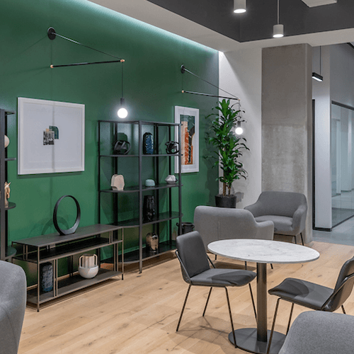 A wall-wash cove fixture delivers uniform illumination along the top of a green accent wall in a contemporary commercial office lounge.