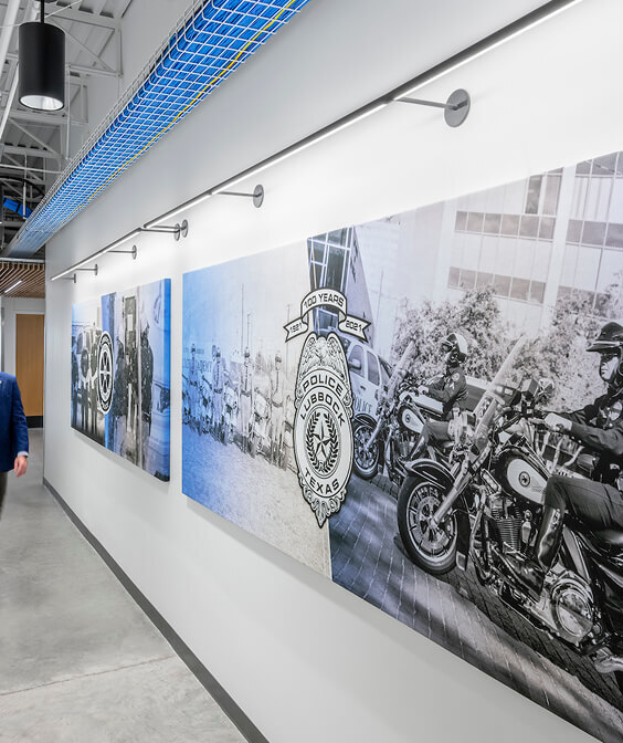 Wall-mounted linear art lights illuminating historical police photographs in a commercial corridor.