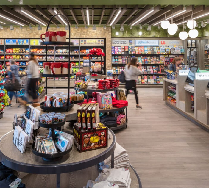 Linear pendant lights fitted into a slatted wooden ceiling provide ambient lighting in an airport retail convenience store.