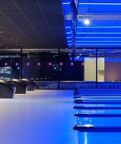 RGBW linear pendant lighting illuminates bowling alley lanes in vibrant blue, creating a cool atmosphere in a modern space.