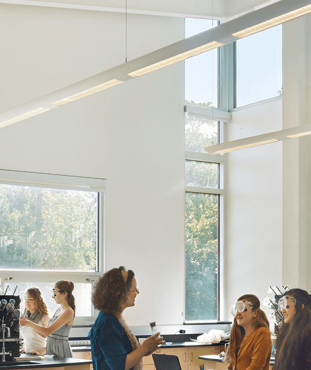 Linear pendant lights installed in continuous runs provide uniform illumination across a classroom lab with worktables and exposed ceiling conditions.