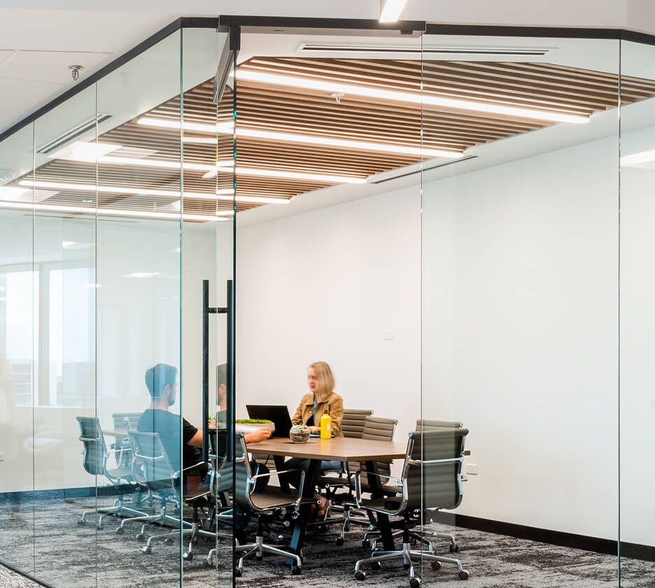 Recessed linear lights set in a slatted wood ceiling over an office conference room table.