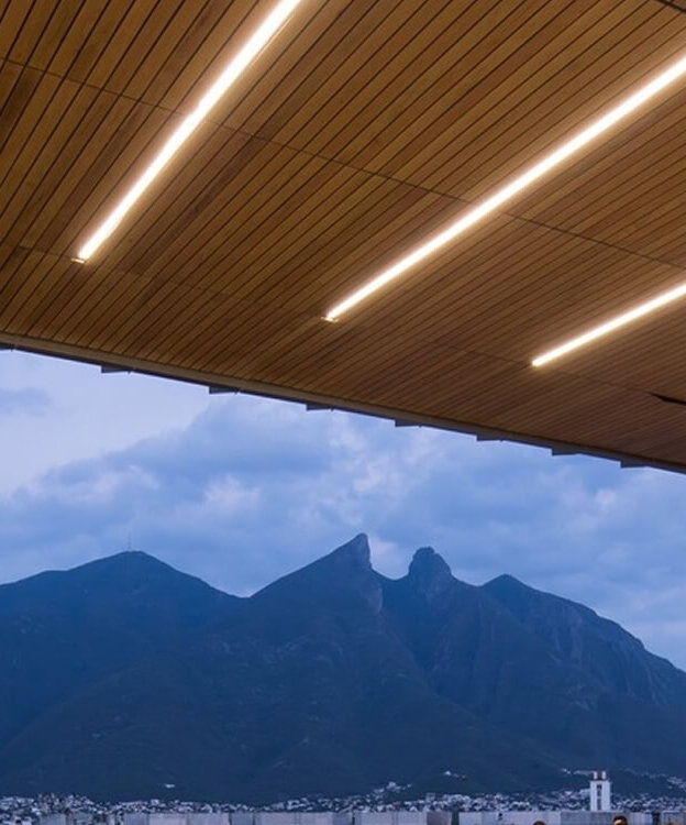 Recessed linear lighting integrated into a wood ceiling illuminates a covered outdoor school patio at night.