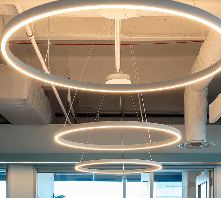 Three slim ring pendant LED lights reduce glare over office workstations with soft direct and indirect lighting.