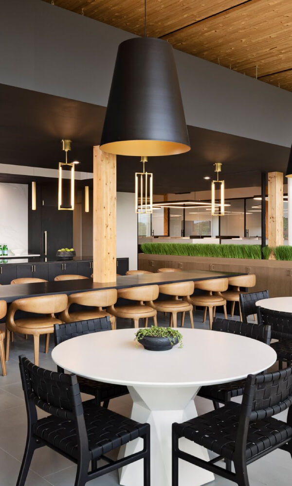 Low bay LED lights illuminate tables in a modern office cafeteria area.