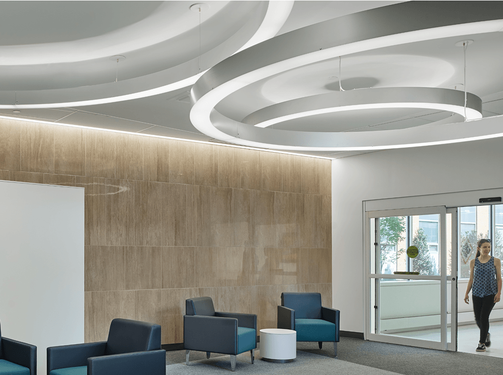 Linear pendant lights installed in continuous runs provide uniform illumination across a classroom lab with worktables and exposed ceiling conditions.