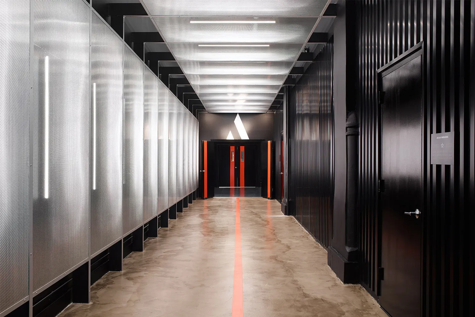 Linear ceiling and wall lights line a corridor leading to an AARMY fitness center with an illuminated logo above the entrance.