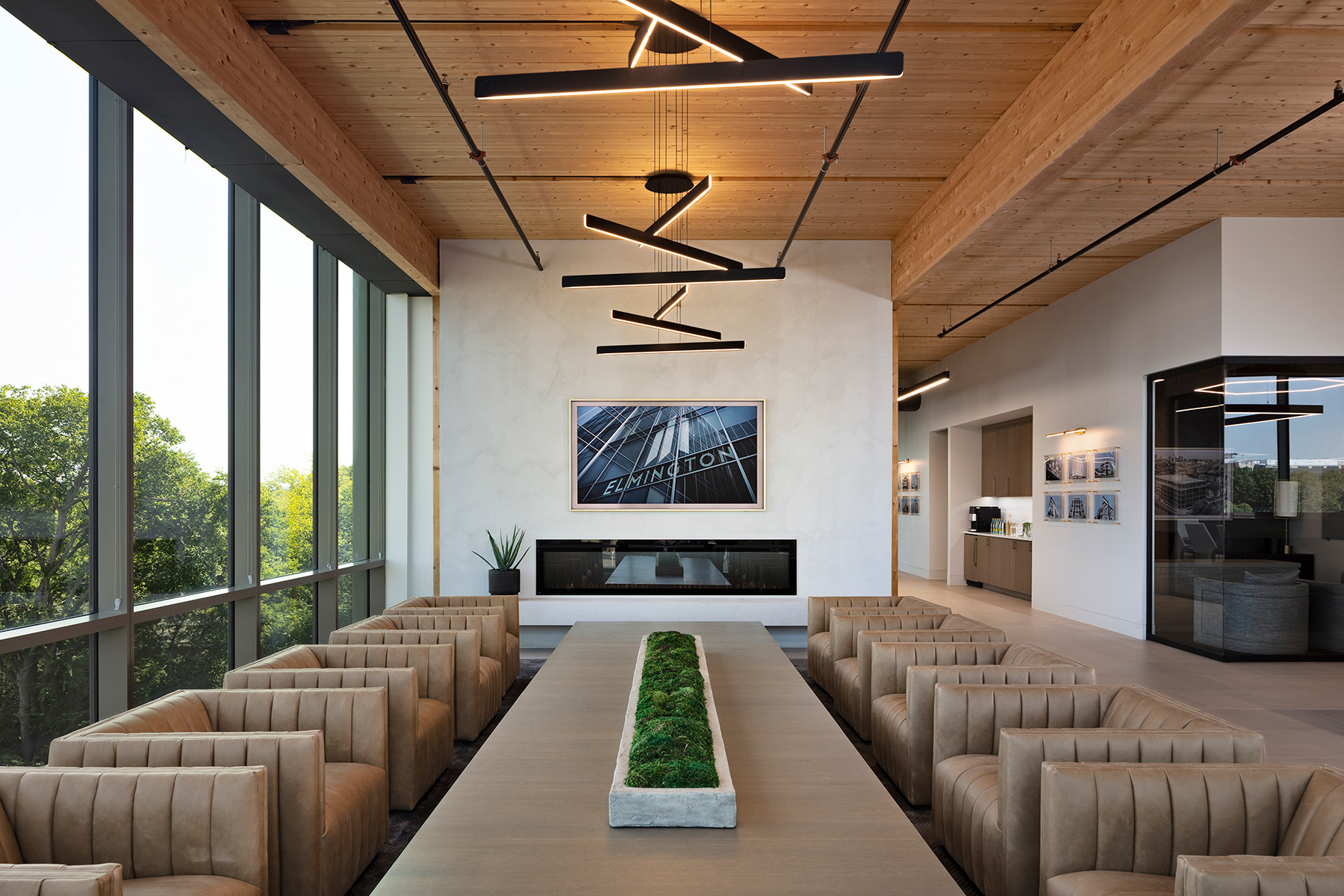 Trios of slim linear LED lights hang at different heights and angles from a single canopy, creating depth and dimension over a casual conference room with an oversized coffee table and eight lounge chairs