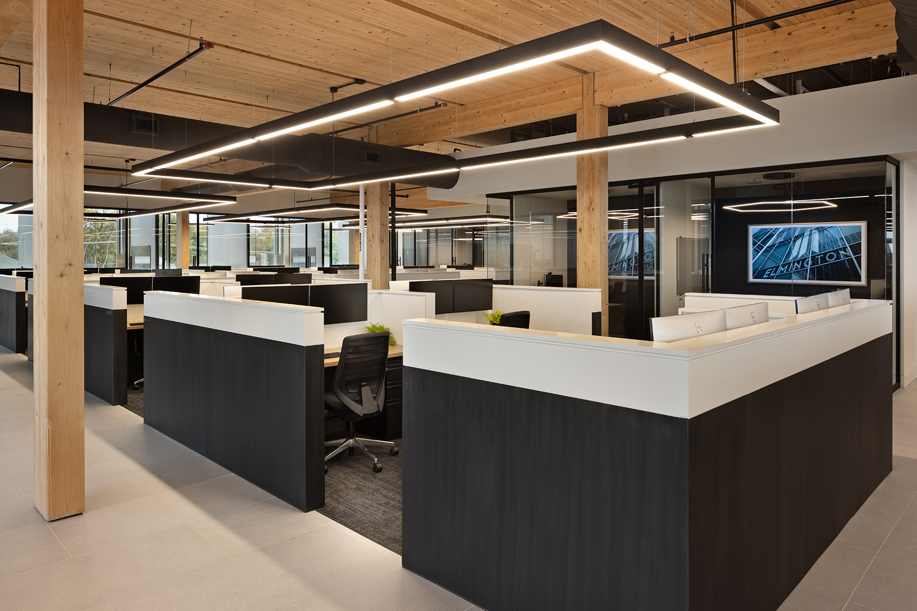 An oversized rectangular LED pendant light suspended by aircraft cables provides general lighting over four workstations in an open floor plan office.