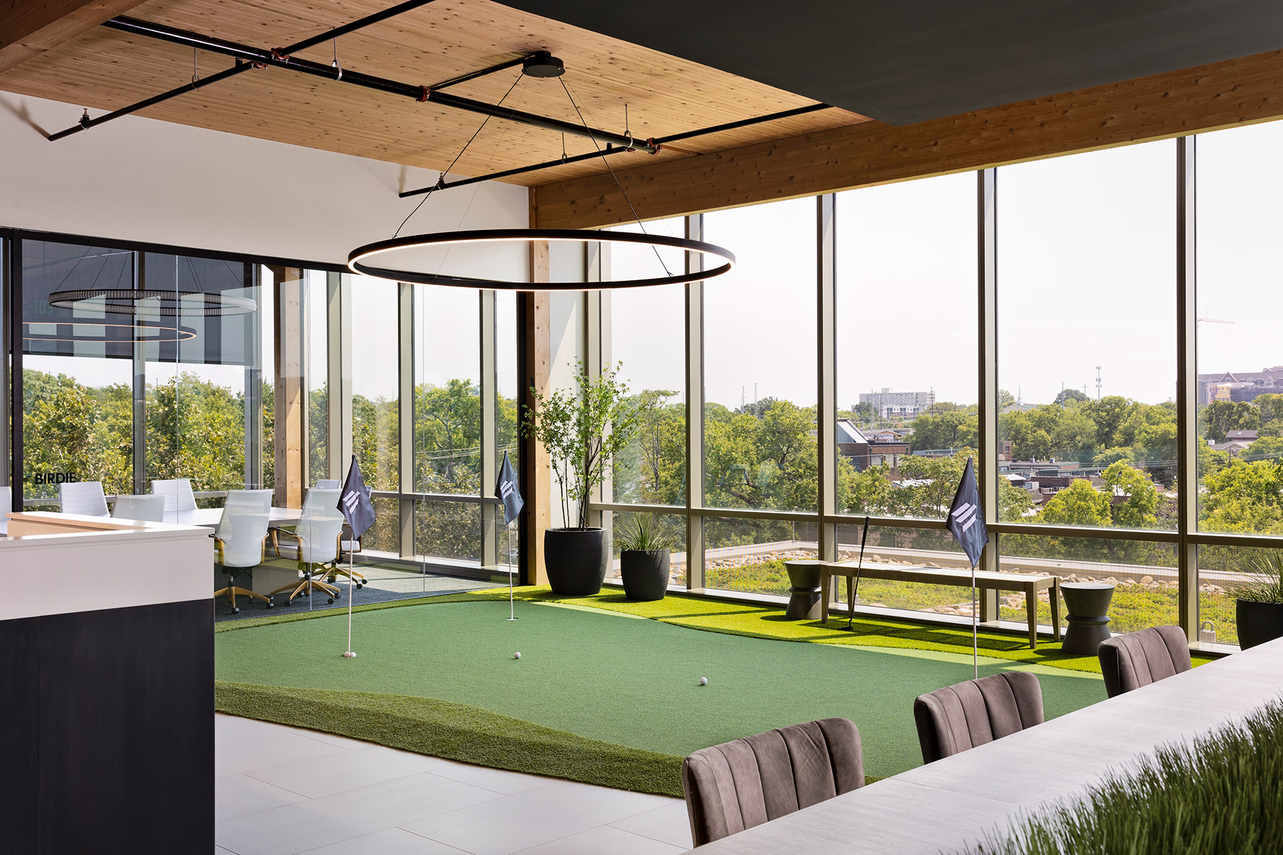 A slim LED ring pendant downlight hangs from a round canopy by adjustable aircraft cable over a putting green break space in a property investment office.
 