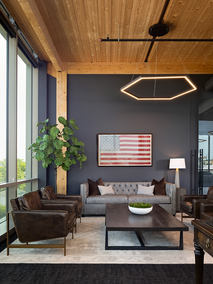 A hexagon LED light pendant hangs from a black round canopy, suspended by adjustable aircraft cables, providing ambient lighting over an office break area with a floor lamp for reading light by a couch.
 