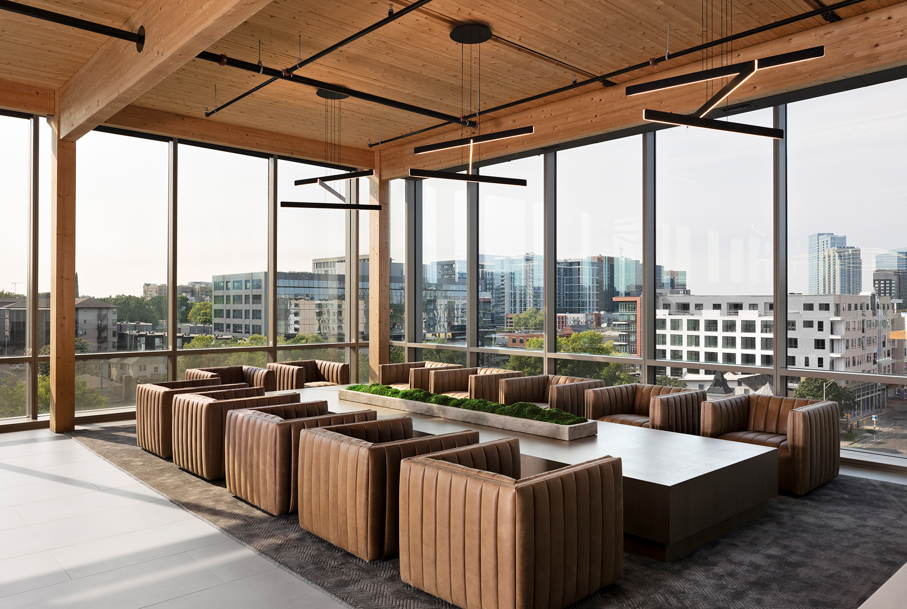 Three LED pendant lights illuminate a casual office conference room. Each fixture has three linear light bars suspended at different heights and angles to create a three-dimensional lighting effect.