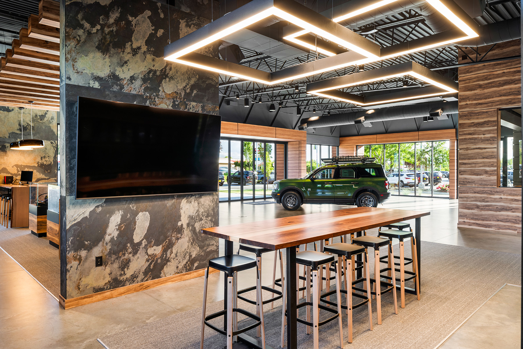Square pendant lights by Alcon Lighting illuminate a conference table and digital screening space in the Kendall Bronco car dealership.