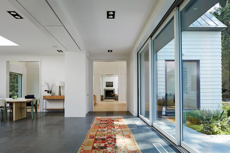 Recessed multiple lights line a hallway in front of floor-to-ceiling windows in a home 