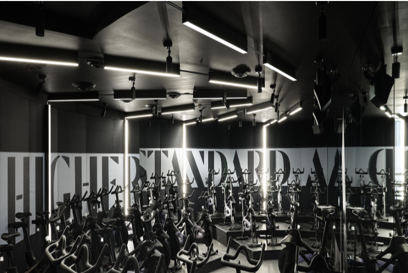 Black linear ceiling and recessed wall lights create an array of lighting simulating a hyperspace jump in a fitness center spin classroom.