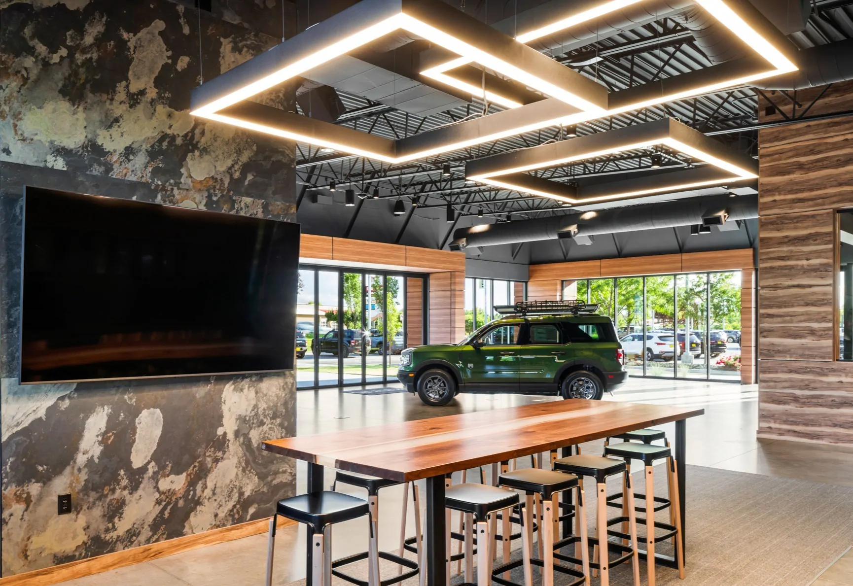 Three modern square pendant lights suspended at varying heights create a focal point over a car showroom conference table.