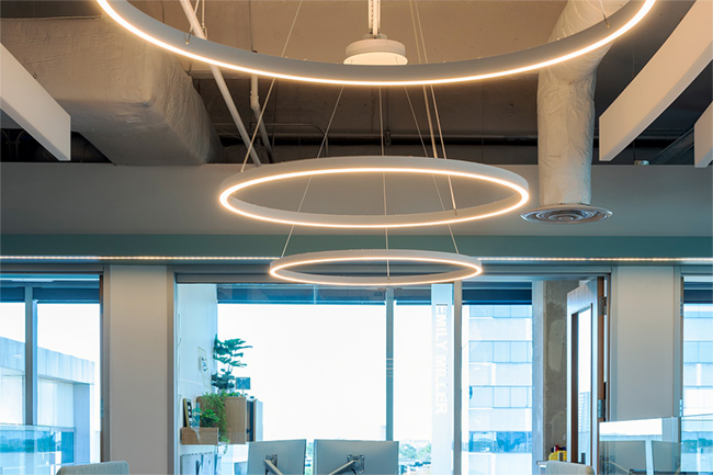 Three oversized ring pendant lights hang over an open floor plan office, providing uplighting and downlighting 