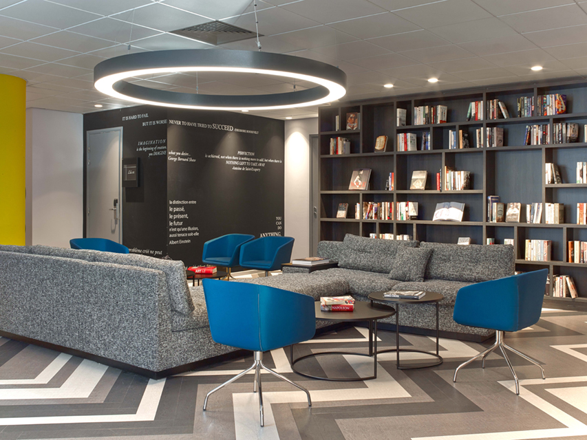 A silver ring pendant light hangs over a reading room area for students at the Le Campus facility