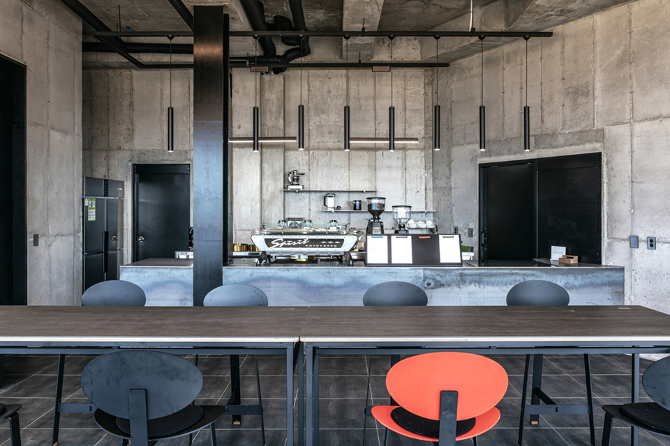 Vertical LED tube pendant lights hang over a coffee bar in a modern office