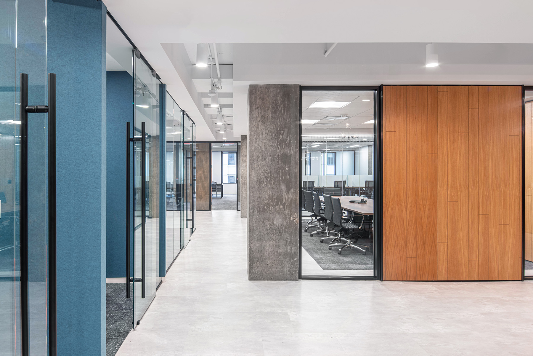 White cylinder pendant lights hang from an exposed ceiling down a corridor between offices and a conference room.