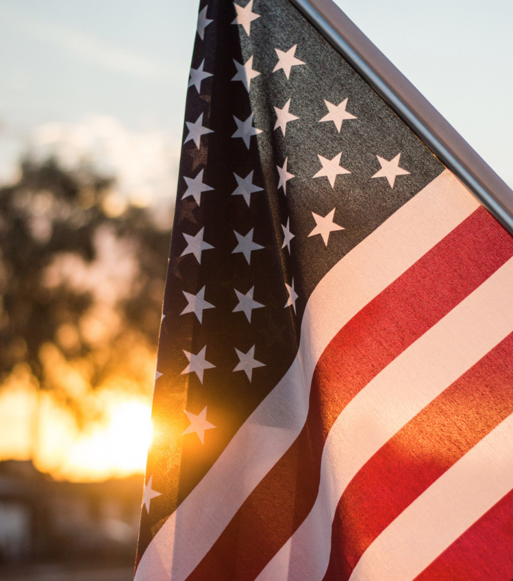 An American flag hangs from a pole in front of a home as the sun rises behind it